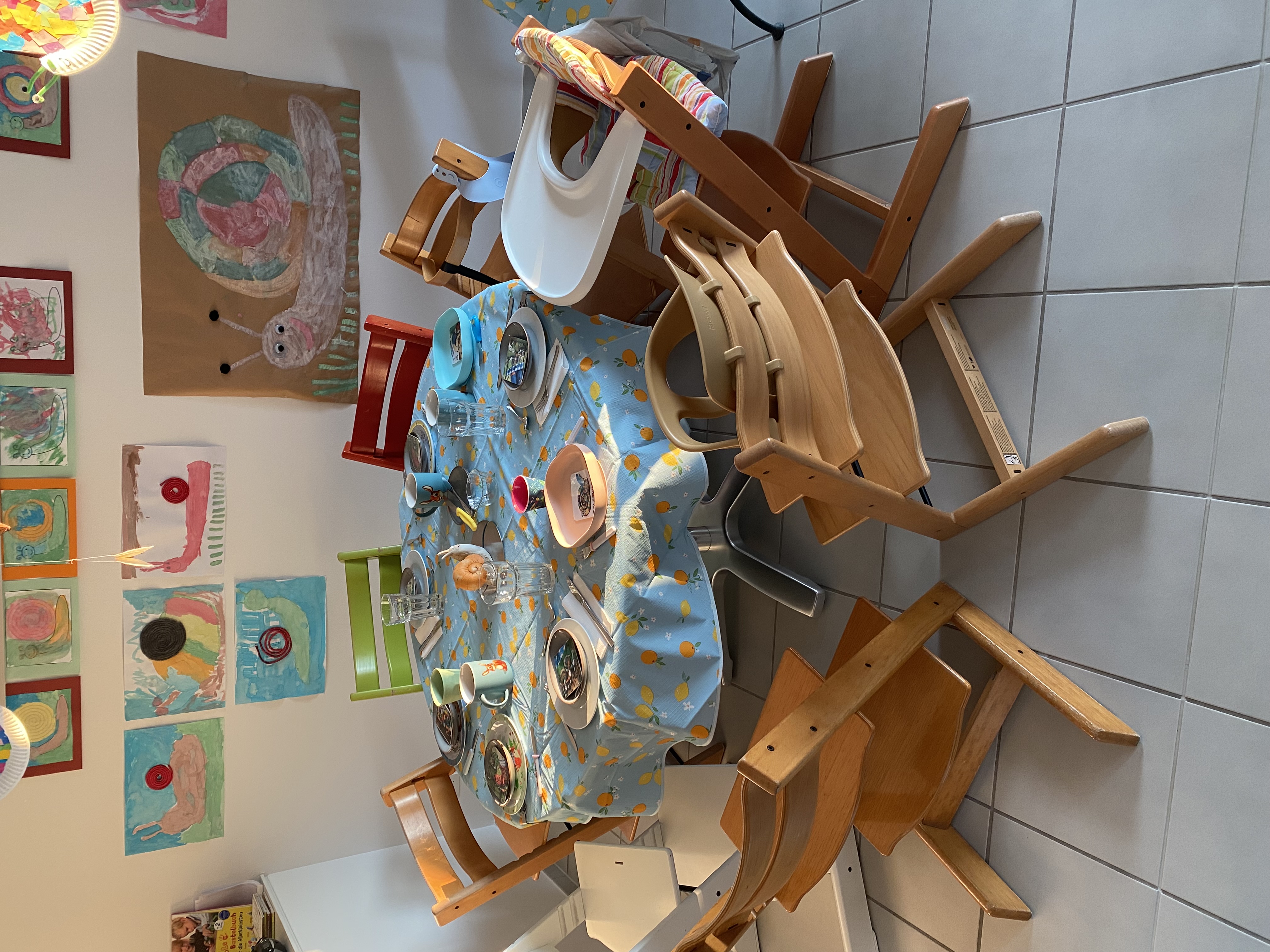 Esstisch mit Kinderstühlen, dekoriert mit Kinderkunst an der Wand
